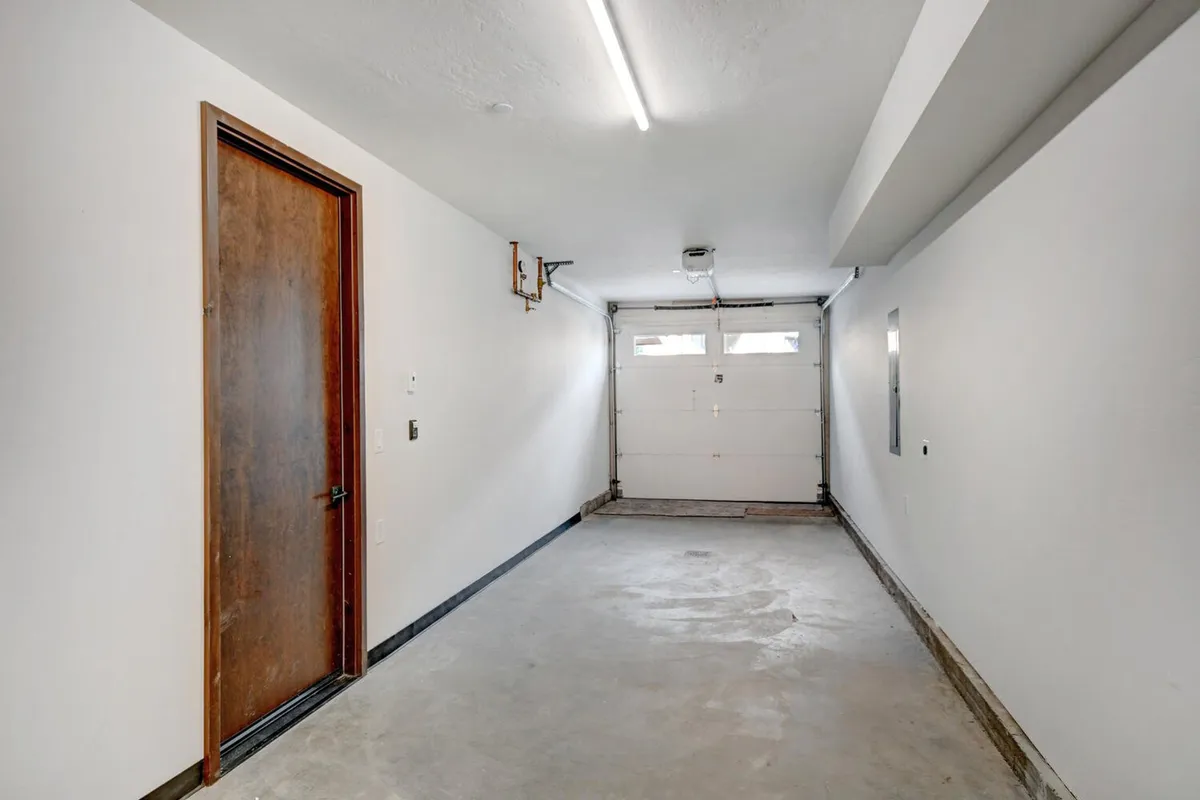 A functional garage space with a visible garage door, side door, and clean walls, suggesting ample room for storing bikes, skis, and other gear. The uncluttered design highlights the storage possibilities and practical entry points.