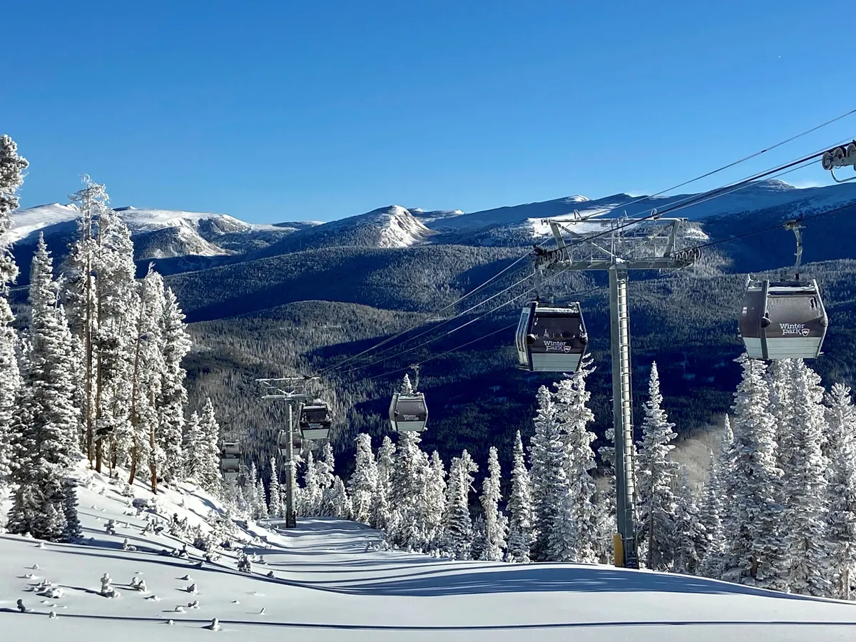 A sweeping exterior view of ski gondolas gliding over snow-covered trees and a vast mountain range. The scene is alive with the promise of winter adventure, highlighting the invigorating environment and easy access to world-class skiing and other snowy pursuits.