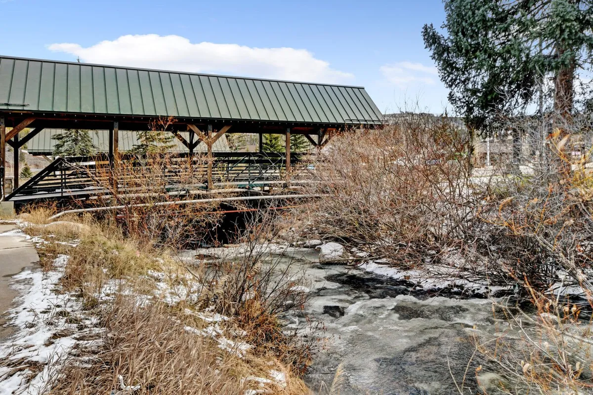 A tranquil exterior shot featuring a wooden bridge spanning a gently flowing creek, surrounded by lush vegetation. The setting feels serene and inviting, ideal for peaceful hikes, trout fishing, and nature observation during spring and fall.