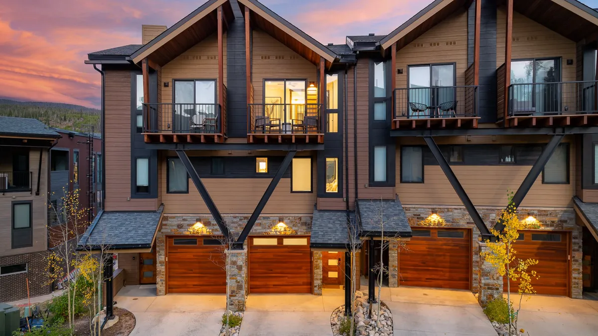 The photo showcases the villa's modern exterior, featuring wooden garage doors, a spacious balcony with seating, and a welcoming entry. The image also nods to the vibrant neighborhood, perfect for family walks and community activities.