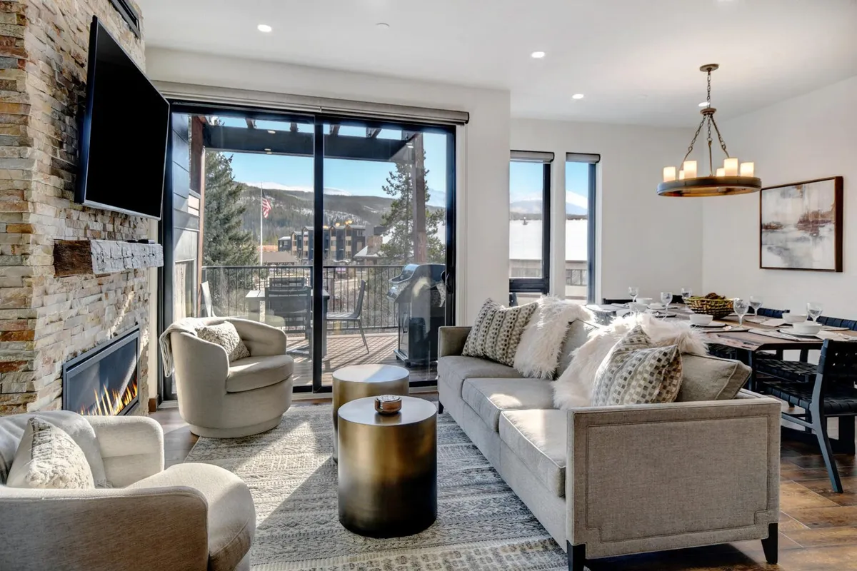 A comfortable living area with a cozy fireplace, large windows letting in natural light, and a spacious dining table. The room feels airy and bright, ideal for socializing, relaxing, or enjoying meals with scenic views.