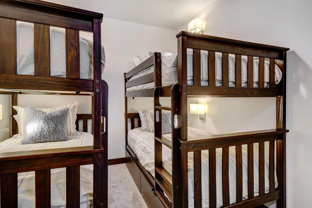 A cheerful bunk room featuring sturdy bunk beds dressed in cozy decorative pillows, wall sconces for evening reading, and a warm inviting vibe. The space feels playful yet comfortable, perfect for children or families.