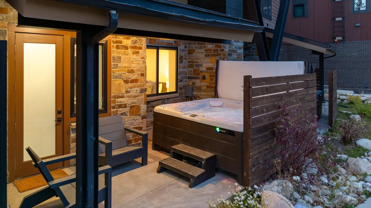 An inviting exterior view showcasing a private hot tub set against a stone wall and comfortable seating, perfect for relaxing or stargazing after an evening out. The scene is tranquil and hints at luxury and exclusivity.