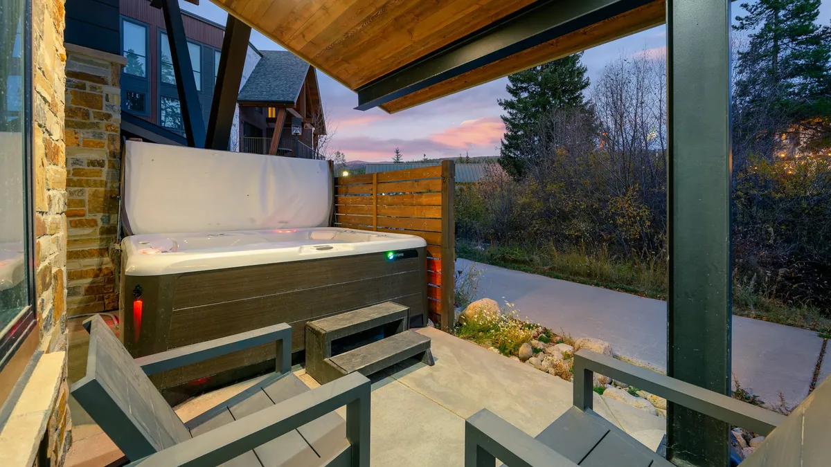 An inviting outdoor hot tub set on a patio, with outdoor seating and lush natural surroundings. The scene evokes relaxation, with a sense of serenity from the integration of nature and a space to unwind after adventure.