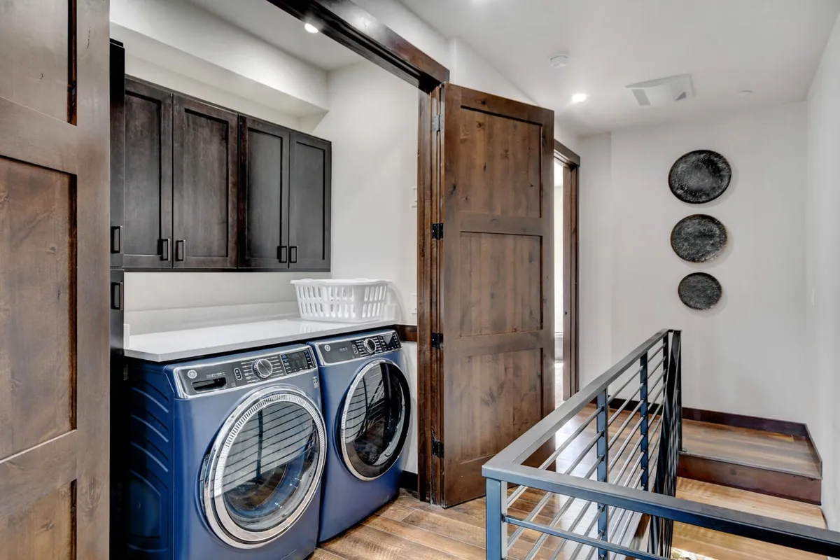 A dedicated laundry area featuring a washer and dryer set, wooden cabinets for organization, and a laundry basket. The space feels tidy and functional, perfect for keeping adventure gear fresh and ready.
