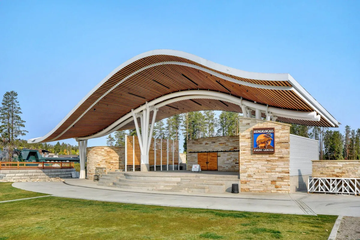 The Hideaway Park amphitheater, featuring a curved roof structure and stone facade, with a prominent stage area ready for concerts, festivals, or community events. The setting suggests lively performances and gatherings.
