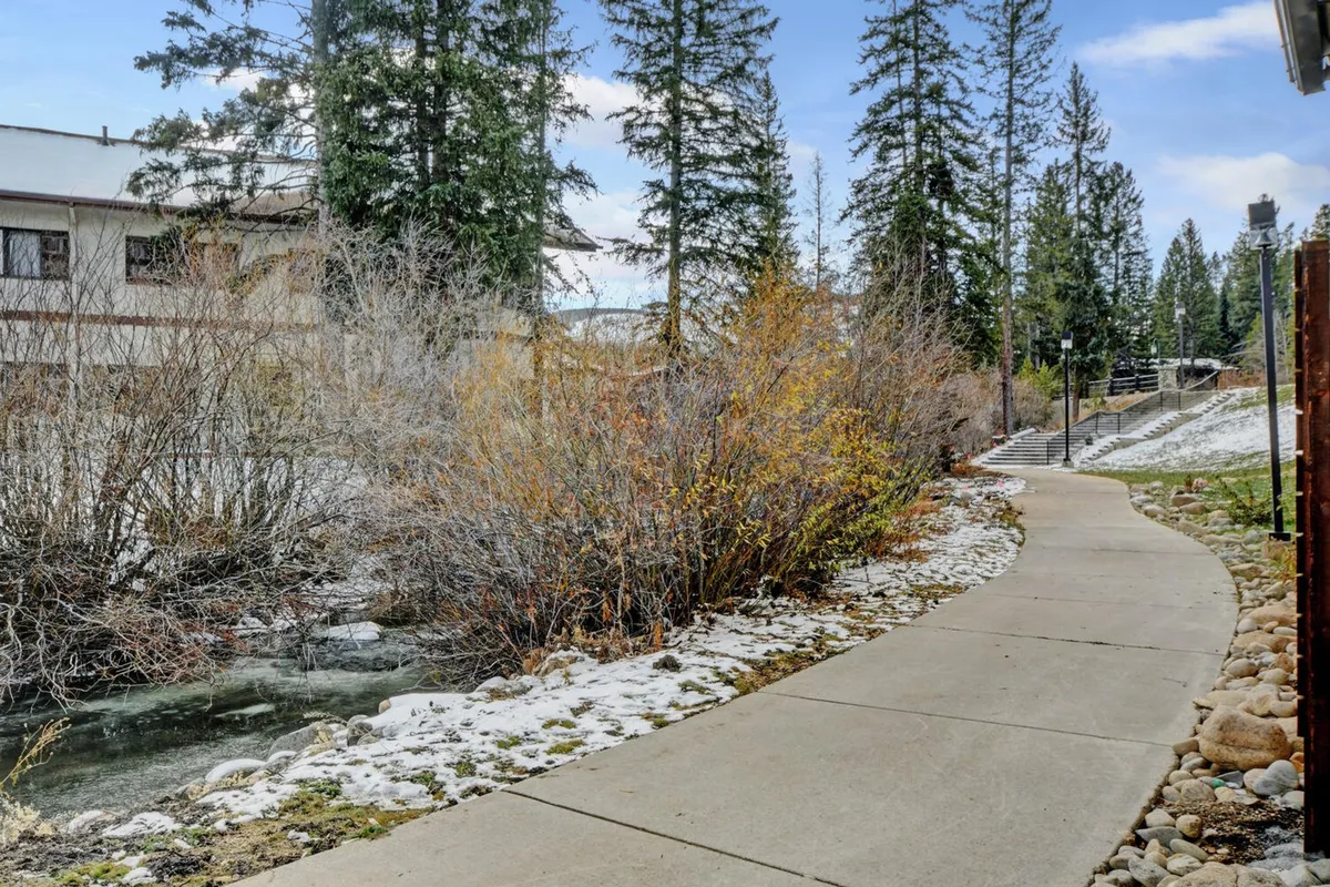 This image shows a winding pathway next to a gently flowing stream, surrounded by lush trees and seasonal foliage. The tranquil setting invites leisurely walks and easy access to nature, making it ideal for families looking to explore the outdoors together.